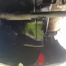 Spód samochodu po nałożeniu grubej warstwy czarnej powłoki ochronnej, widoczna rura wydechowa i elementy zawieszenia.