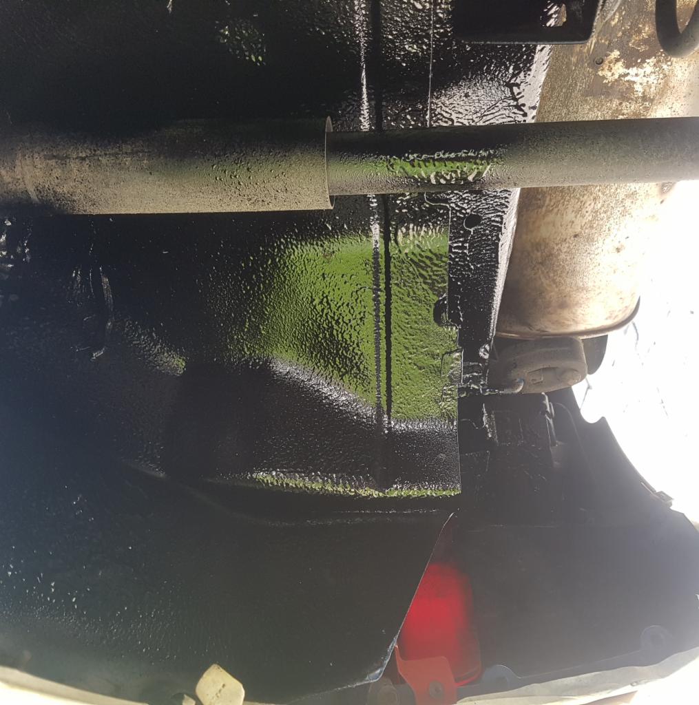 Spód samochodu po nałożeniu grubej warstwy czarnej powłoki ochronnej, widoczna rura wydechowa i elementy zawieszenia.