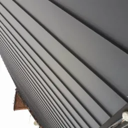 Świeżo położone, szare blaszane pokrycie dachowe z widocznym fragmentem starej ceglanej konstrukcji i narzędziem do montażu w prawym dolnym rogu.