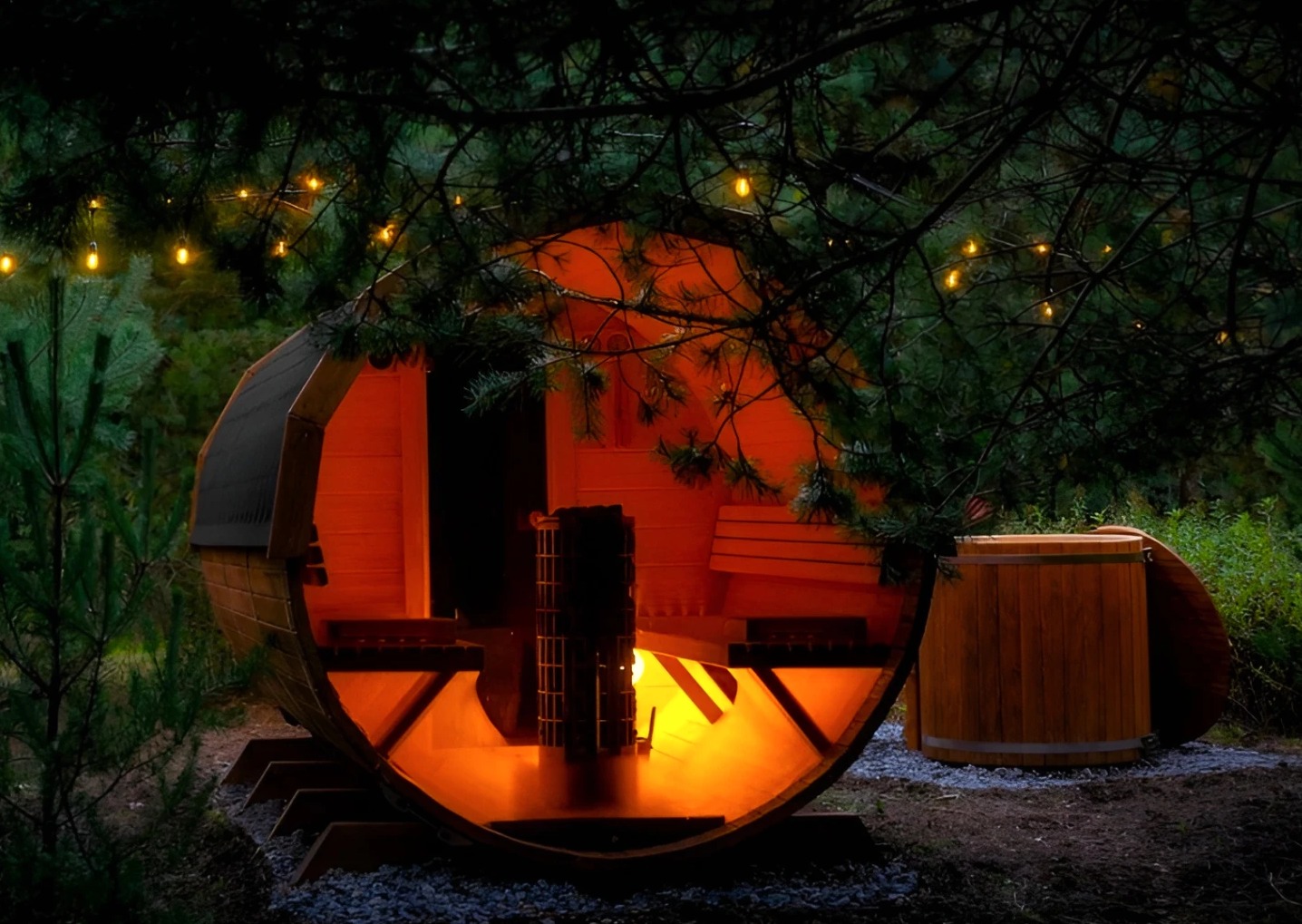 Okrągła sauna beczka z oświetleniem w lesie, widok na wnętrze z piecem i ławkami, obok drewniana balia. Nastrojowe oświetlenie tworzy ciepłą atmosferę.