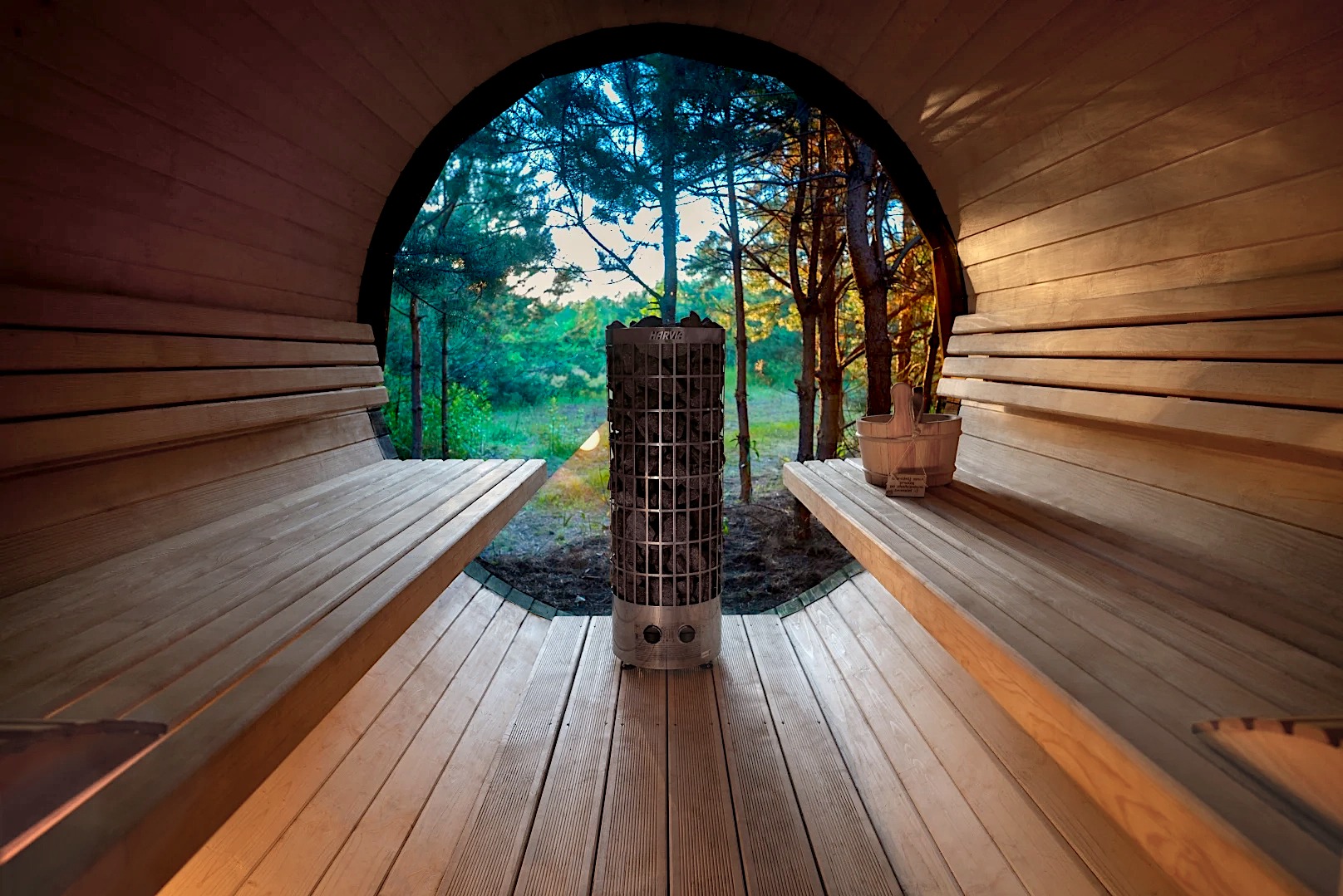 Drewniana sauna beczka z piecem Harvia na kamienie, widok na las. Naturalne światło, relaksująca atmosfera.