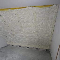 Izolacje Natryskowe Kielczyk Rafał Rafpur - Poddasze po ociepleniu pianką PUR, widoczne mocowania, żółta warstwa izolacyjna przy suficie, surowy beton na podłodze, ściany przygotowane do wykończenia.