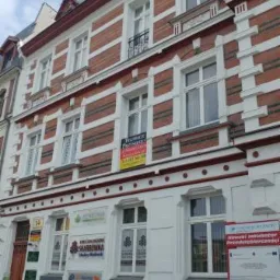 Elewacja kamienicy z biurami, widoczne szyldy i reklamy firm, w tym szyld z napisem SKARBOWNIKA i logo z drzewem.