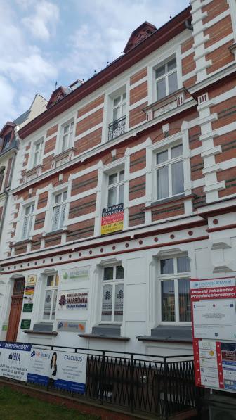 Elewacja kamienicy z biurami, widoczne szyldy i reklamy firm, w tym szyld z napisem SKARBOWNIKA i logo z drzewem.