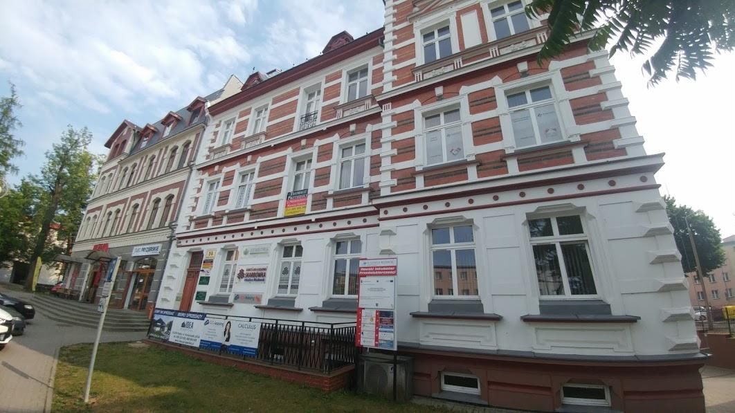 Budynek biurowy z szyldami firm, w tym biura rachunkowego, z widocznymi oknami i architekturą z czerwonej cegły.