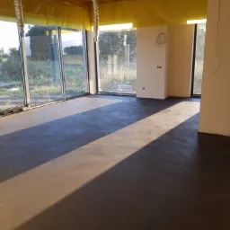 Wnętrze w stanie deweloperskim w Myszkowie z wylaną, gładką wylewką podłogową, duże okna z widokiem na zewnątrz, przygotowane do dalszych prac wykończeniowych.