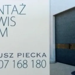 Tablica reklamowa z napisem 'Montaż Serwis Bram' i danymi kontaktowymi firmy Mateusz Piecka, obok widoczna zamknięta, szara brama segmentowa z poziomymi panelami.