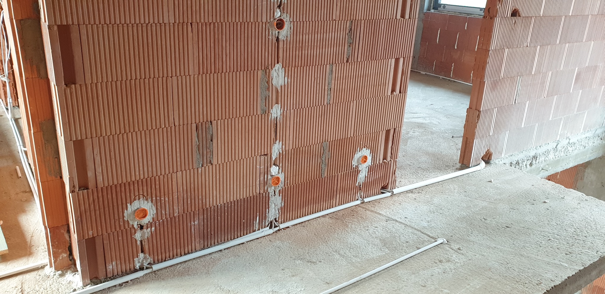 Wewnętrzna ściana z pustaków ceramicznych z wywierconymi otworami i osadzonymi puszkami instalacyjnymi, zabezpieczonymi gipsem, oraz ułożonymi na podłodze rurkami peszel.