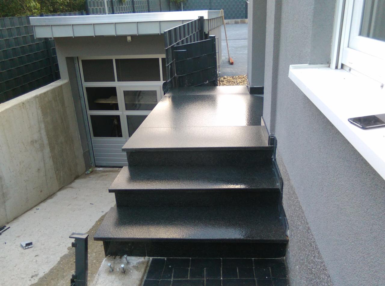 Zewnętrzne schody wyłożone czarnymi, błyszczącymi płytkami, prowadzące do garażu; widoczne detale wykończenia i faktura płytek.