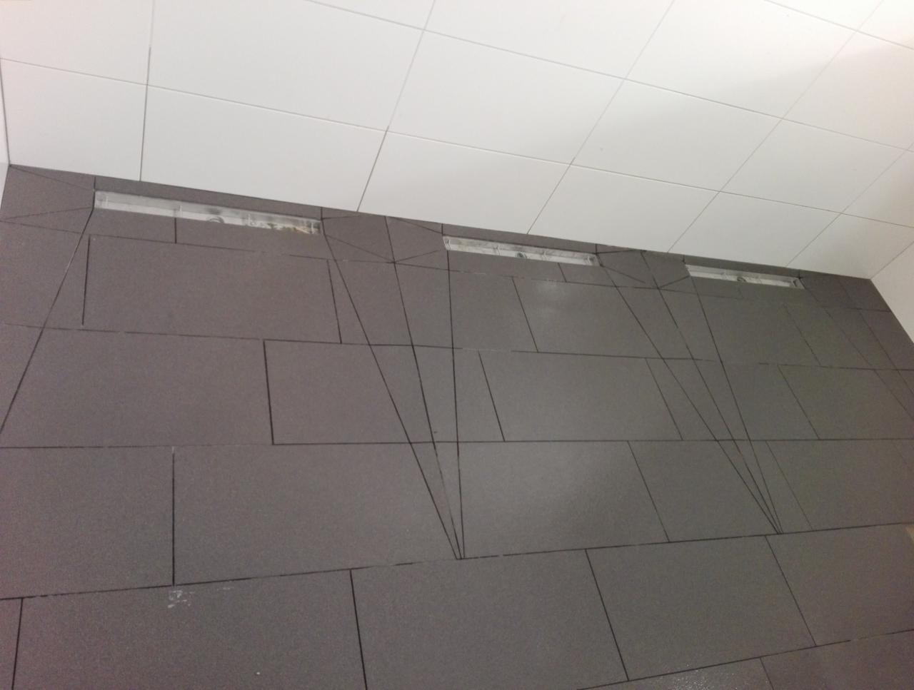 Ściana z szarych płytek ceramicznych z widocznymi liniami fugi, górna krawędź ściany z elementami oświetleniowymi, biały sufit z kwadratowych płytek