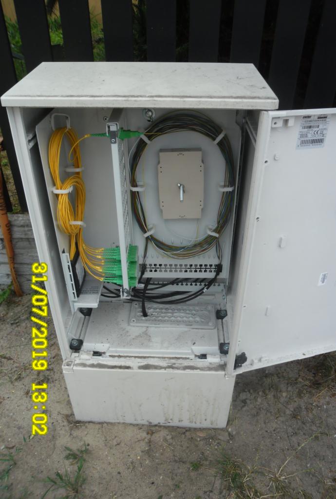 Otwarta, zewnętrzna skrzynka telekomunikacyjna z widoczną instalacją światłowodową i przewodami wewnątrz.