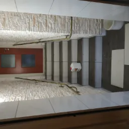 Klatka schodowa w trakcie prac: ściana wykończona dekoracyjną okładziną kamienną, schody z płytkami w odcieniach szarości i bieli, poręcz z metalu w kolorze złotym, widoczny pojemnik z klejem...