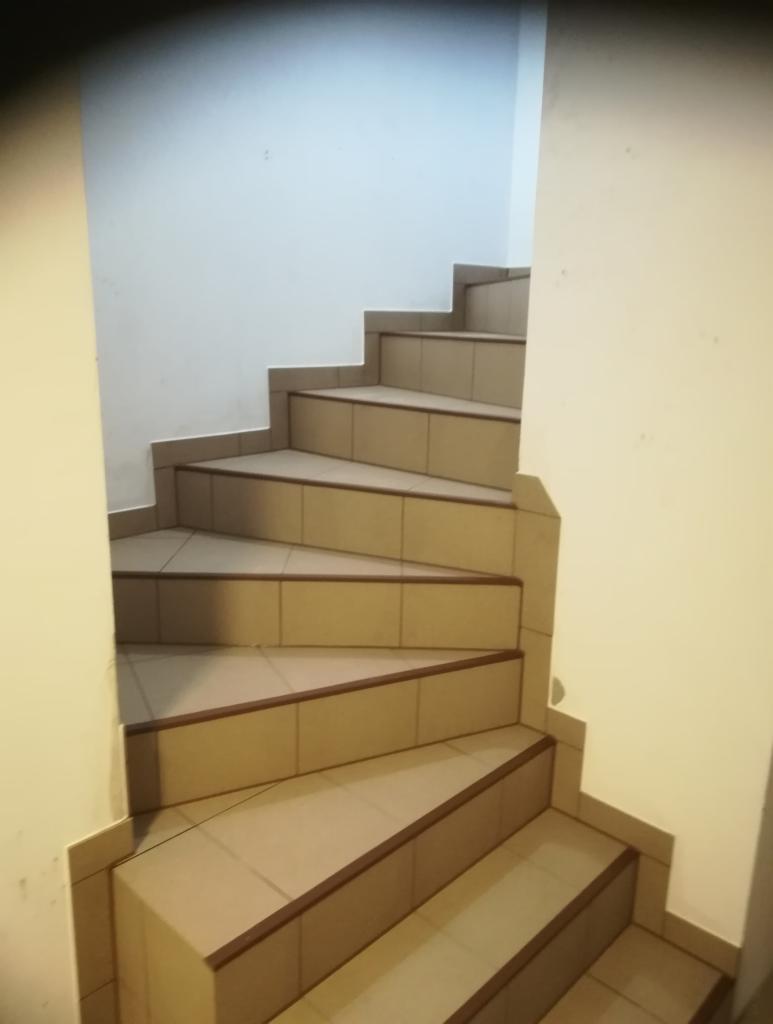 Wewnętrzne, spiralne schody wyłożone beżowymi płytkami z brązowymi krawędziami, prowadzące w górę w jasnym pomieszczeniu.