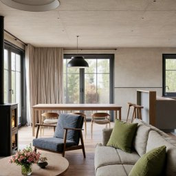 JELCONSULTING SP. Z O.O. - Jasne wnętrze z kominkiem, drewnianym stołem i szarą sofą z zielonymi poduszkami. Minimalistyczny design z ceglanym akcentem i dużymi oknami.