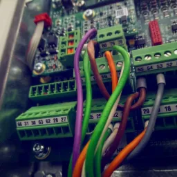 Szczegółowe ujęcie panelu elektrycznego z kolorowymi przewodami podłączonymi do zielonych złączek, widoczne numery identyfikacyjne na złączkach i elementy elektroniczne na płytce drukowanej.