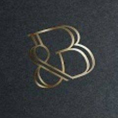 Złoty, stylizowany monogram 'B&' na ciemnym, matowym tle, oświetlony z góry.