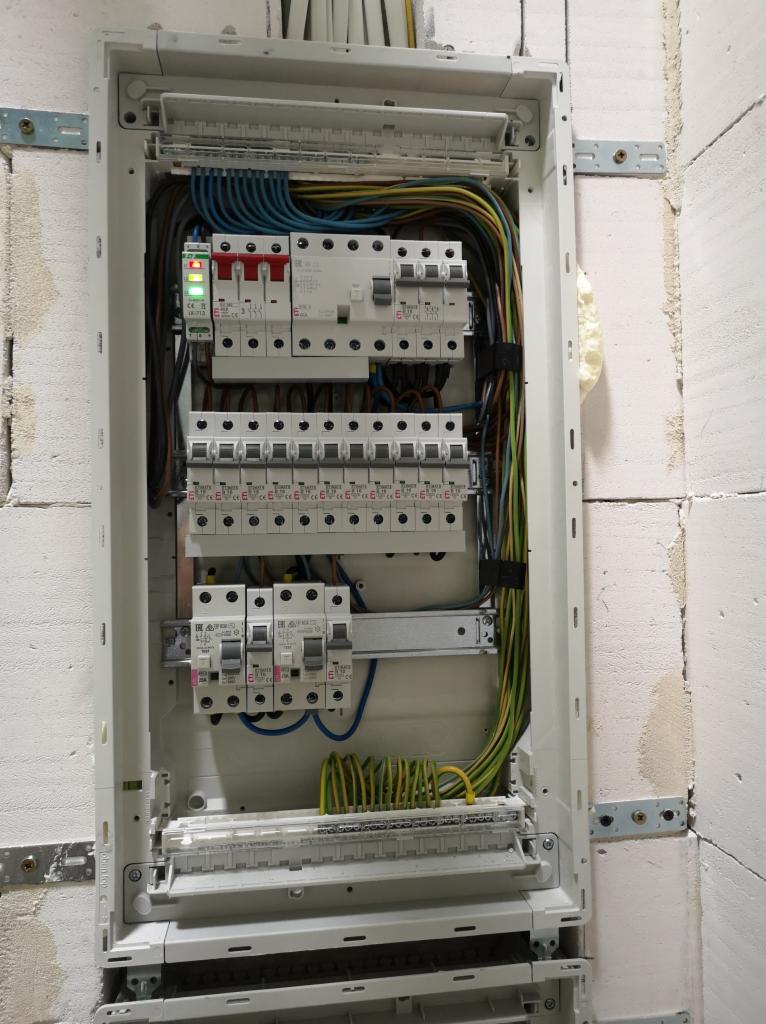 Rozdzielnica elektryczna z zainstalowanymi bezpiecznikami i przewodami, zamontowana na ścianie z bloków, widoczne elementy mocujące. Instalacja zabezpieczeń.