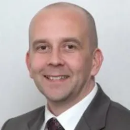 Uśmiechnięty mężczyzna w garniturze, z krótkimi włosami, prezentujący profesjonalny wizerunek. Portret biznesowy.