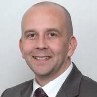 Uśmiechnięty mężczyzna w garniturze, z krótkimi włosami, prezentujący profesjonalny wizerunek. Portret biznesowy.