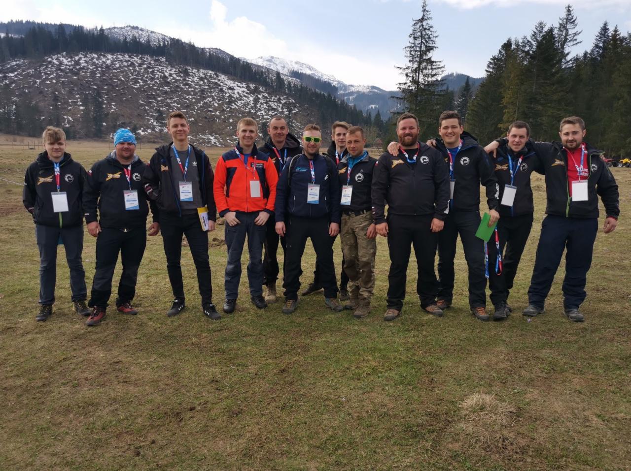 Grupa mężczyzn w Witowie, prawdopodobnie uczestników lub organizatorów wydarzenia plenerowego, pozuje na tle łąki i gór z resztkami śniegu, ubrani w jednakowe kurtki z identyfikatorami.