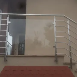 Zewnętrzna balustrada ze stali nierdzewnej i szkła na schodach wejściowych do budynku, widok z dołu na szarą, pochmurną pogodę.