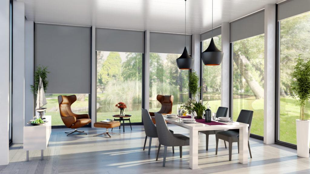 Nowoczesne wnętrze jadalni z dużymi oknami, zasłoniętymi szarymi materiałowymi osłonami przeciwsłonecznymi, widok na park z jeziorkiem.