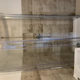 Wykończona łazienka z kabiną prysznicową z przezroczystego szkła, beżowe płytki imitujące drewno na ścianach i podłodze, biała umywalka.