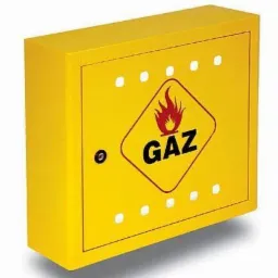 Żółta szafka gazowa z symbolem płomienia w czerwonym rombie i napisem GAZ, widoczne otwory wentylacyjne i zamek.