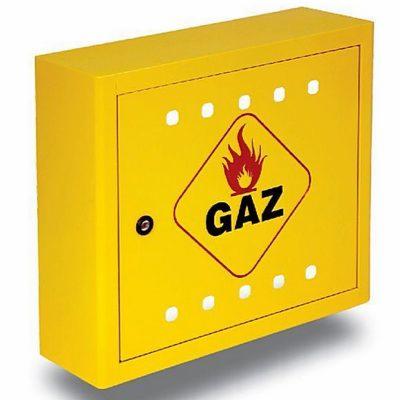 Żółta szafka gazowa z symbolem płomienia w czerwonym rombie i napisem GAZ, widoczne otwory wentylacyjne i zamek.
