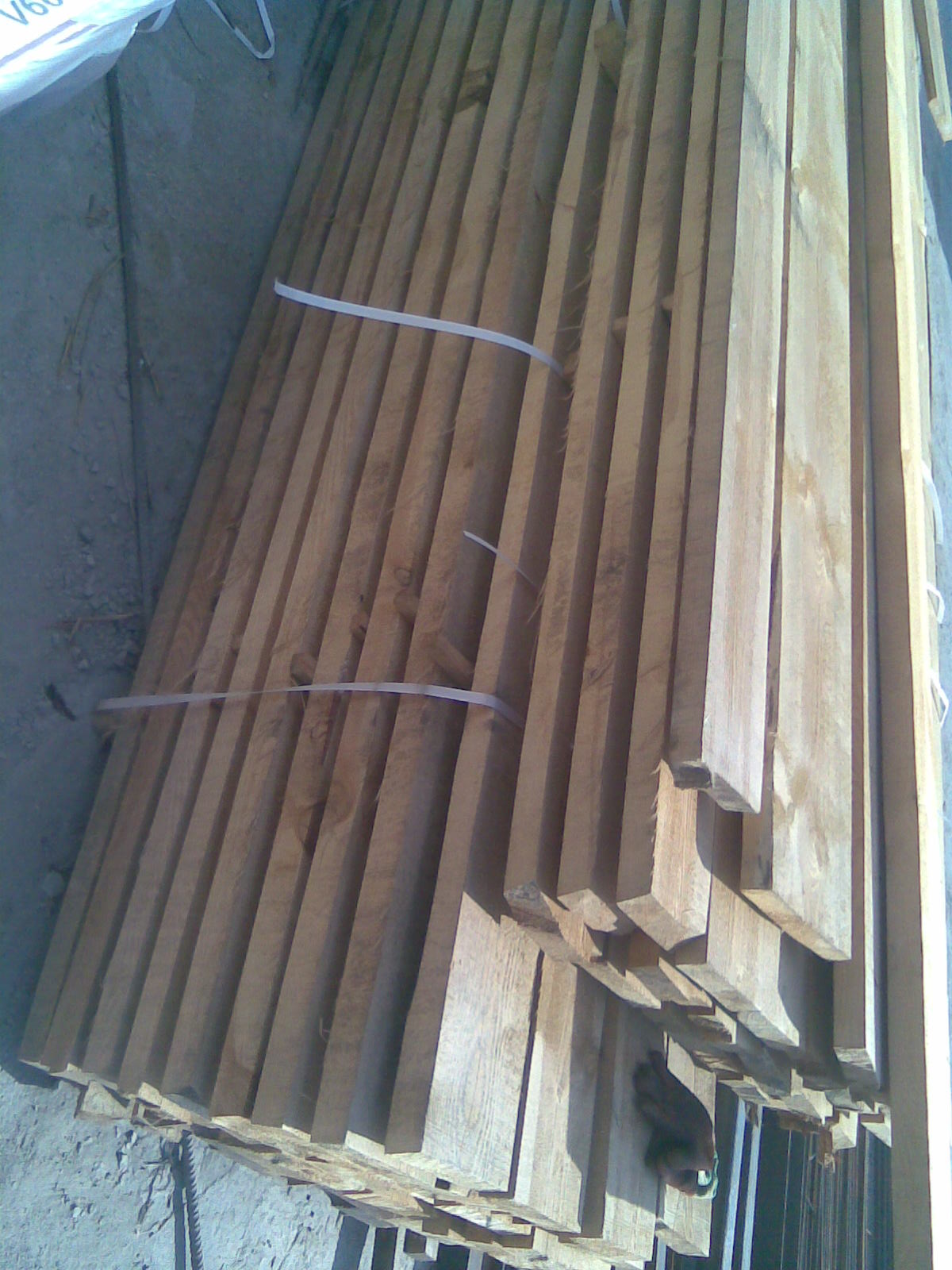 Stos tarcicy budowlanej, związany taśmami, widoczny z góry pod kątem, z widocznymi fragmentami nierównego podłoża.