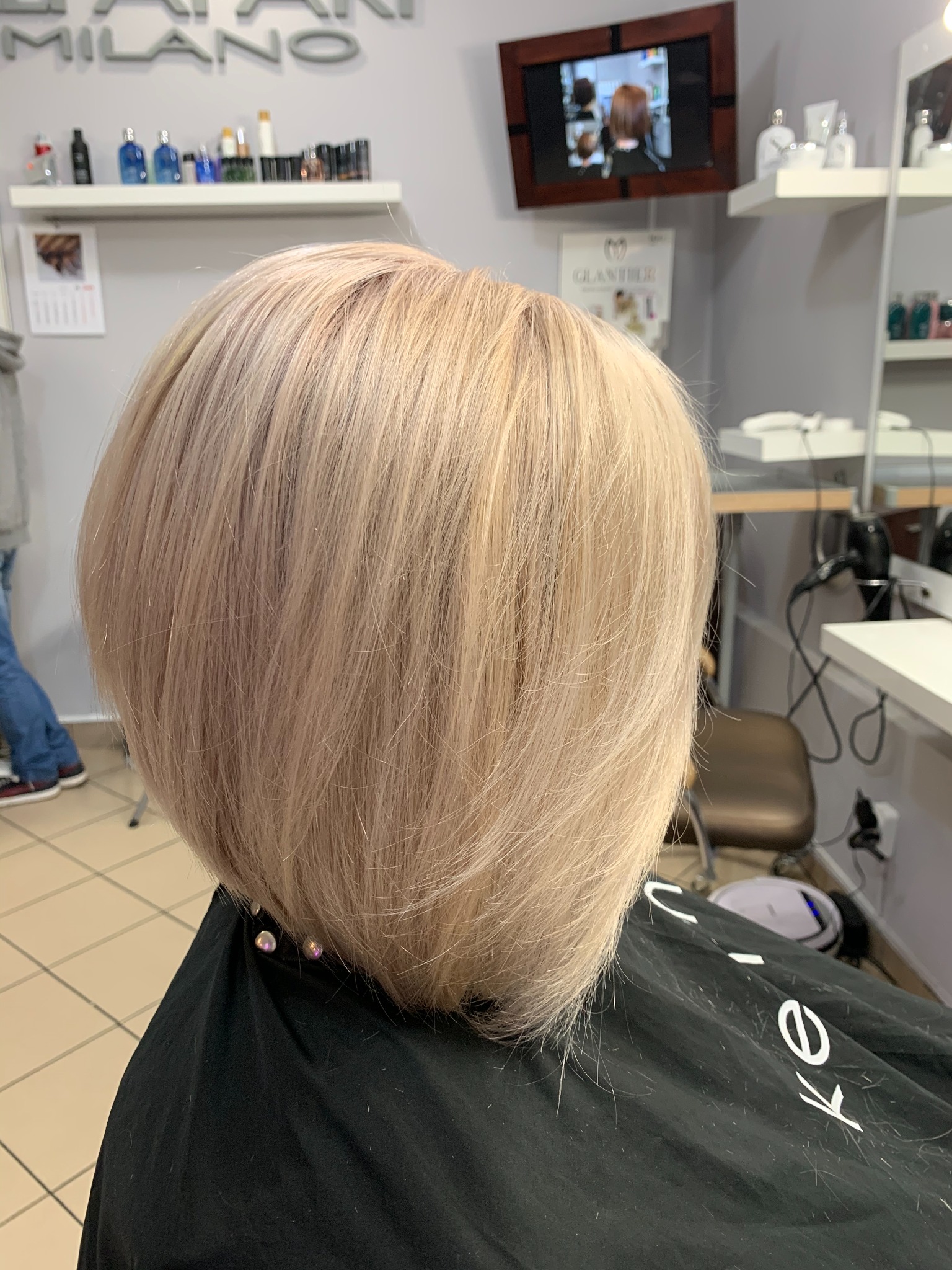 Krótkie, blond włosy z delikatnym fioletowym odcieniem, świeżo po strzyżeniu w salonie fryzjerskim, widoczne resztki włosów na pelerynie.