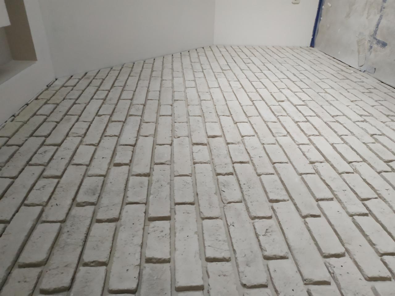 Biała, ceglana podłoga ułożona w jodełkę w nowym wnętrzu, z widocznymi śladami zaprawy i surowym wykończeniem ścian.