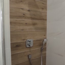 ArtHome - Nowoczesna kabina prysznicowa z drewnopodobnymi panelami ściennymi, chromowana armatura, deszczownica i szklane drzwi.