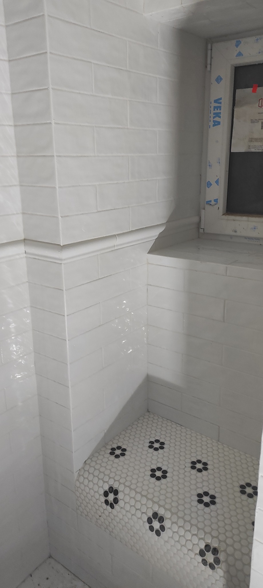 Wykończony fragment łazienki we Wrocławiu z białymi, prostokątnymi płytkami ułożonymi w cegiełkę oraz mozaiką podłogową z czarno-białym wzorem kwiatowym na półce.