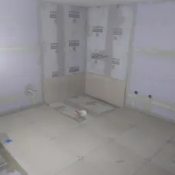 Układanie jasnych płytek podłogowych w łazience w Cisewie, widoczne krzyżyki dystansowe i narzędzia glazurnicze, ściany przygotowane pod płytki z widocznymi oznaczeniami producenta.