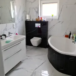 Nowoczesna łazienka z biało-czarnymi marmurowymi płytkami, podwieszaną toaletą, białą umywalką z szafką i owalną wanną z czarną obudową.
