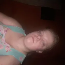 Portret kobiety w bluzce w kwiaty na ciemnym tle, sfotografowanej pod nietypowym kątem.