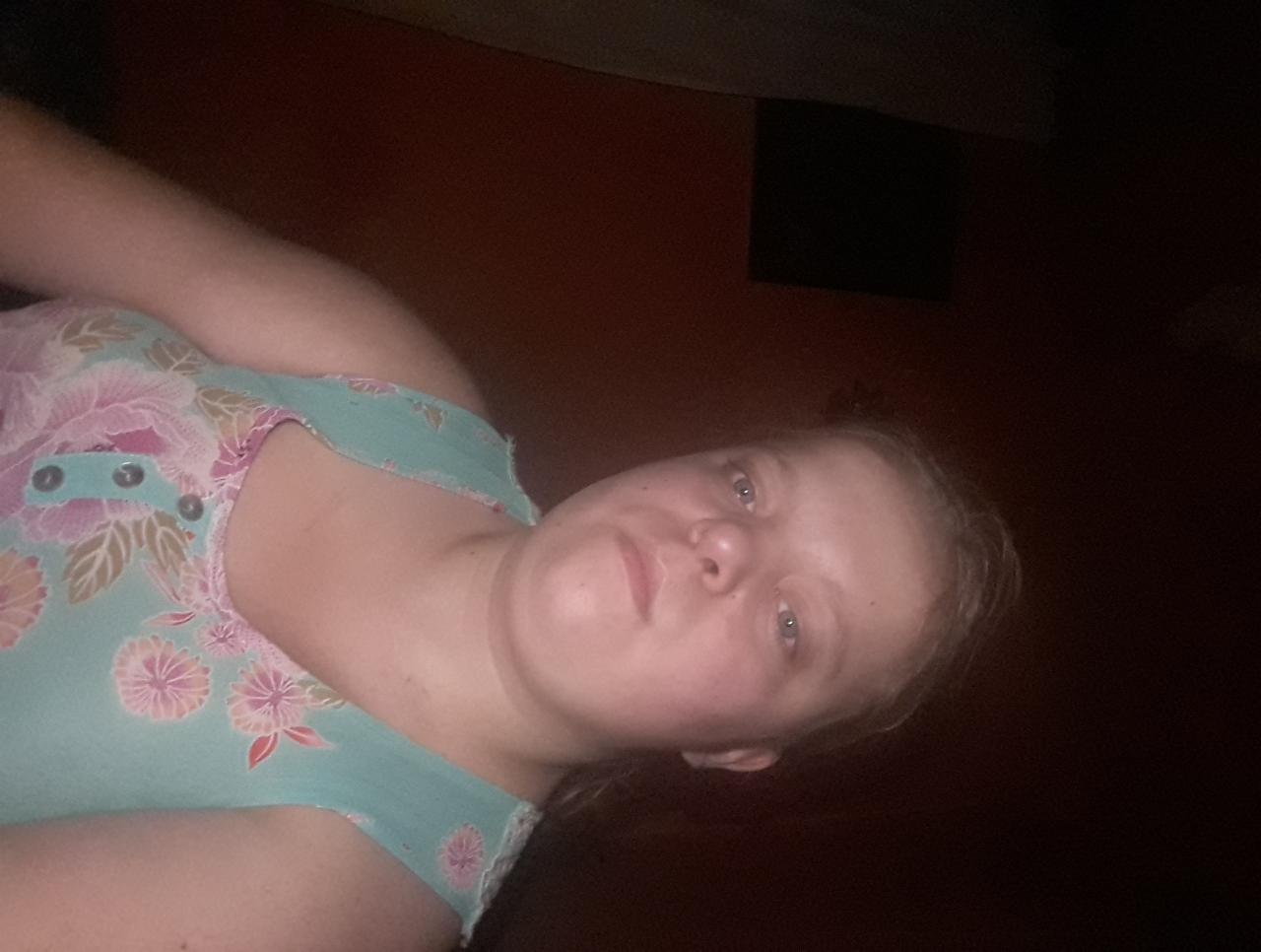 Portret kobiety w bluzce w kwiaty na ciemnym tle, sfotografowanej pod nietypowym kątem.