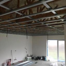 Parlament - Montaż sufitu podwieszanego z widoczną konstrukcją metalową i przewodami elektrycznymi, w tle ściany przygotowane do malowania i okno balkonowe.