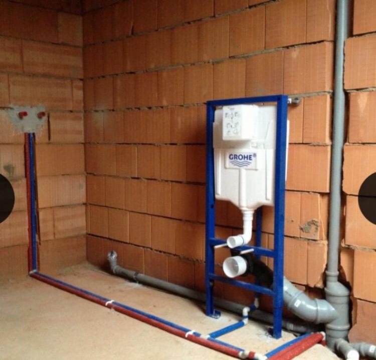 Stelaż podtynkowy Grohe zamontowany przy ścianie z cegły, widoczne rury doprowadzające wodę z niebiesko-czerwonym oznaczeniem.