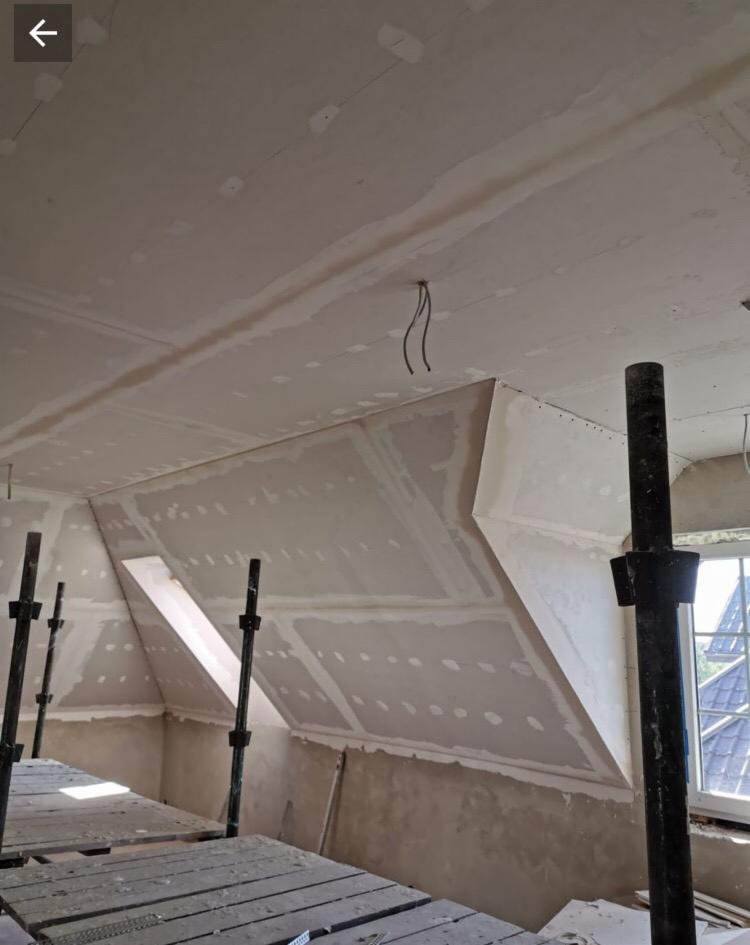 Poddasze w trakcie montażu płyt gipsowo-kartonowych, widoczne rusztowanie, okno dachowe i wystające kable elektryczne z sufitu.