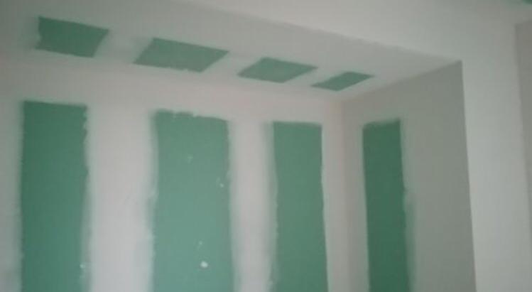 Ściana i sufit w trakcie szpachlowania, widoczne pionowe pasy szpachli na ścianie i kwadratowe wypełnienia na suficie, przygotowanie do malowania.