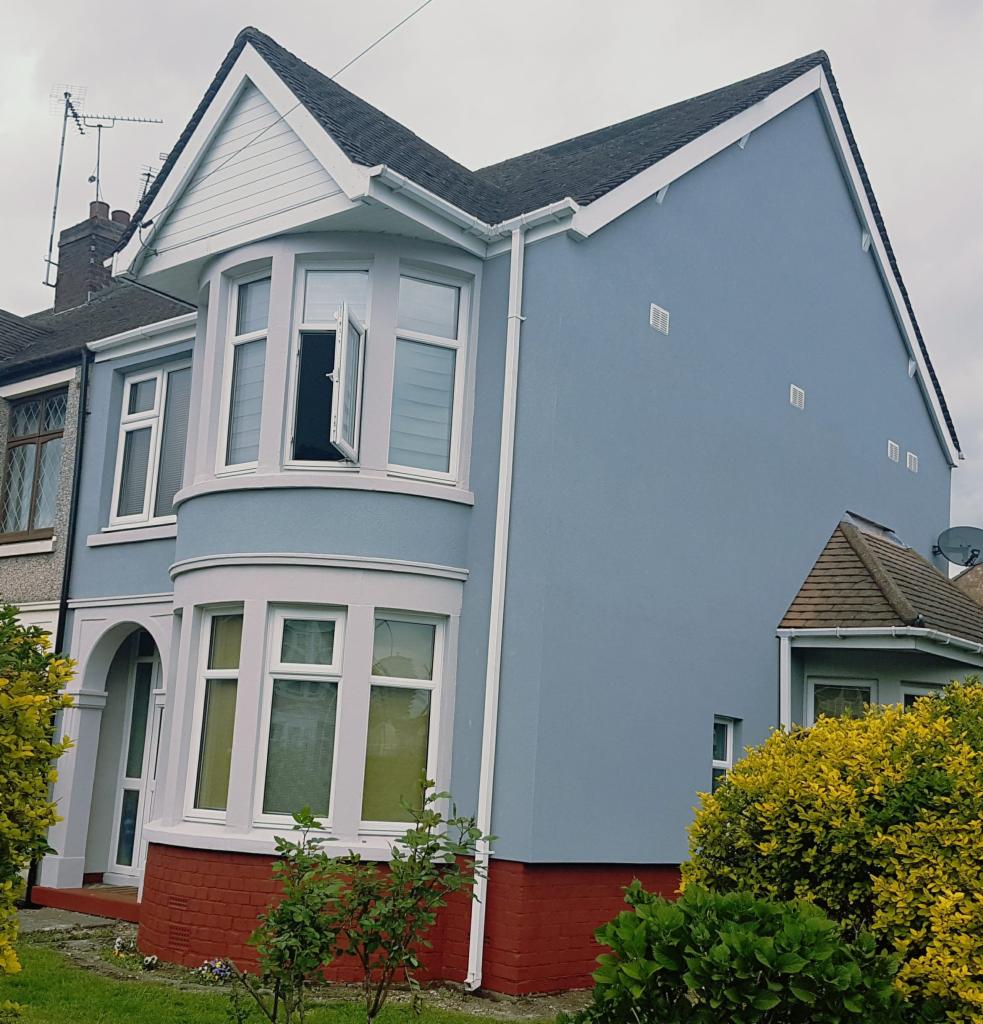 Odnowiona elewacja dwukondygnacyjnego domu z zaokrąglonym wykuszem, świeżo otynkowana na pastelowy błękit, z otwartym oknem w wykuszu i czerwoną cegłą w dolnej części elewacji.