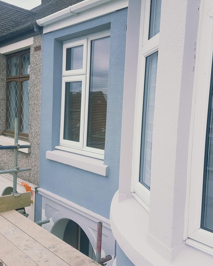 Fragment elewacji budynku po tynkowaniu, z widocznym rusztowaniem i oknami z białymi ramami. Na sąsiedniej ścianie widoczna elewacja z fakturą i oknem z brązową ramą.