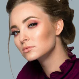 Portret kobiety z upiętymi włosami ozdobionymi błyszczącymi spinkami, w bordowej bluzce z wiązaniem przy szyi i z profesjonalnym makijażem oczu w odcieniach różu.