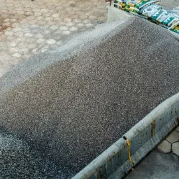 Góra drobnego, szarego kruszywa w betonowym boksie, obok worki z materiałem i palety z zapakowanym towarem, widok z góry.