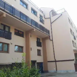 Nowoczesny budynek wielorodzinny z beżową elewacją, balkonami z czarnymi balustradami i widocznym systemem rynnowym.