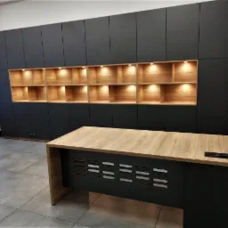 Biuro z zabudową ścienną w kolorze grafitowym z podświetlanymi półkami z jasnego drewna i biurkiem z blatem imitującym drewno.