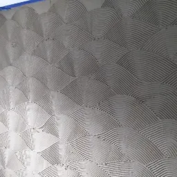 Ściana pokryta świeżo nałożoną, szarą gładzią z wyraźnym wzorem fal ułożonych jeden nad drugim.