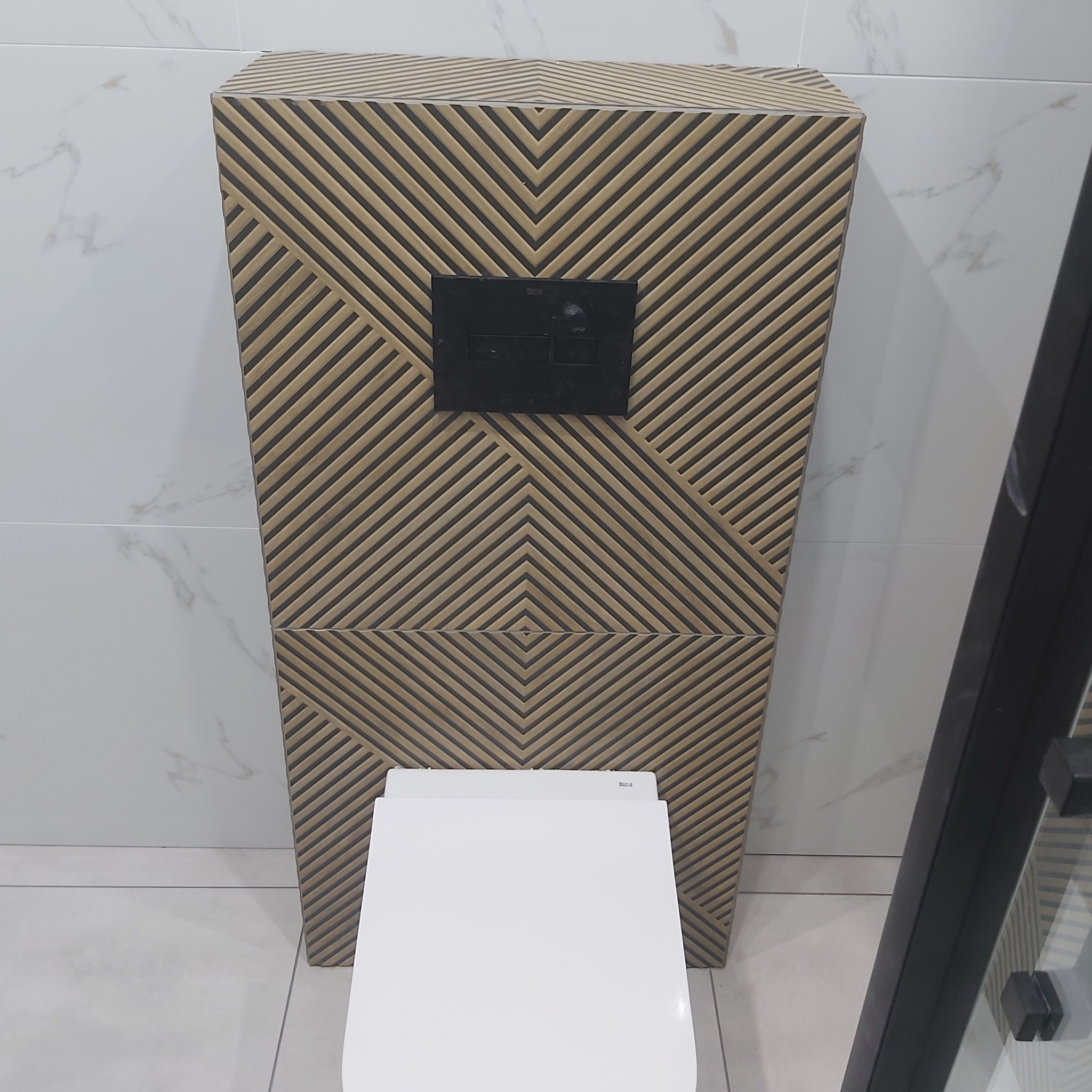 Nowoczesna toaleta podwieszana z geometryczną obudową, czarny panel sterujący spłukiwaniem, białe marmurowe płytki ścienne